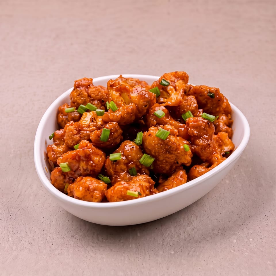 A white bowl filled with orange-glazed cauliflower florets, garnished with chopped green onions.